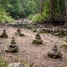 Rock cairns in a dry australian riverbed, with surrounding bushland and trees visible in the background.