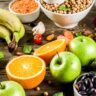 Assorted carbohydrate rich foods including bananas, apples, oranges, beans, lentils, bread and nuts on a wooden table.