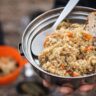 Hiker holding a metal bowl of quinoa and beans with bread during a backcountry meal stop.
