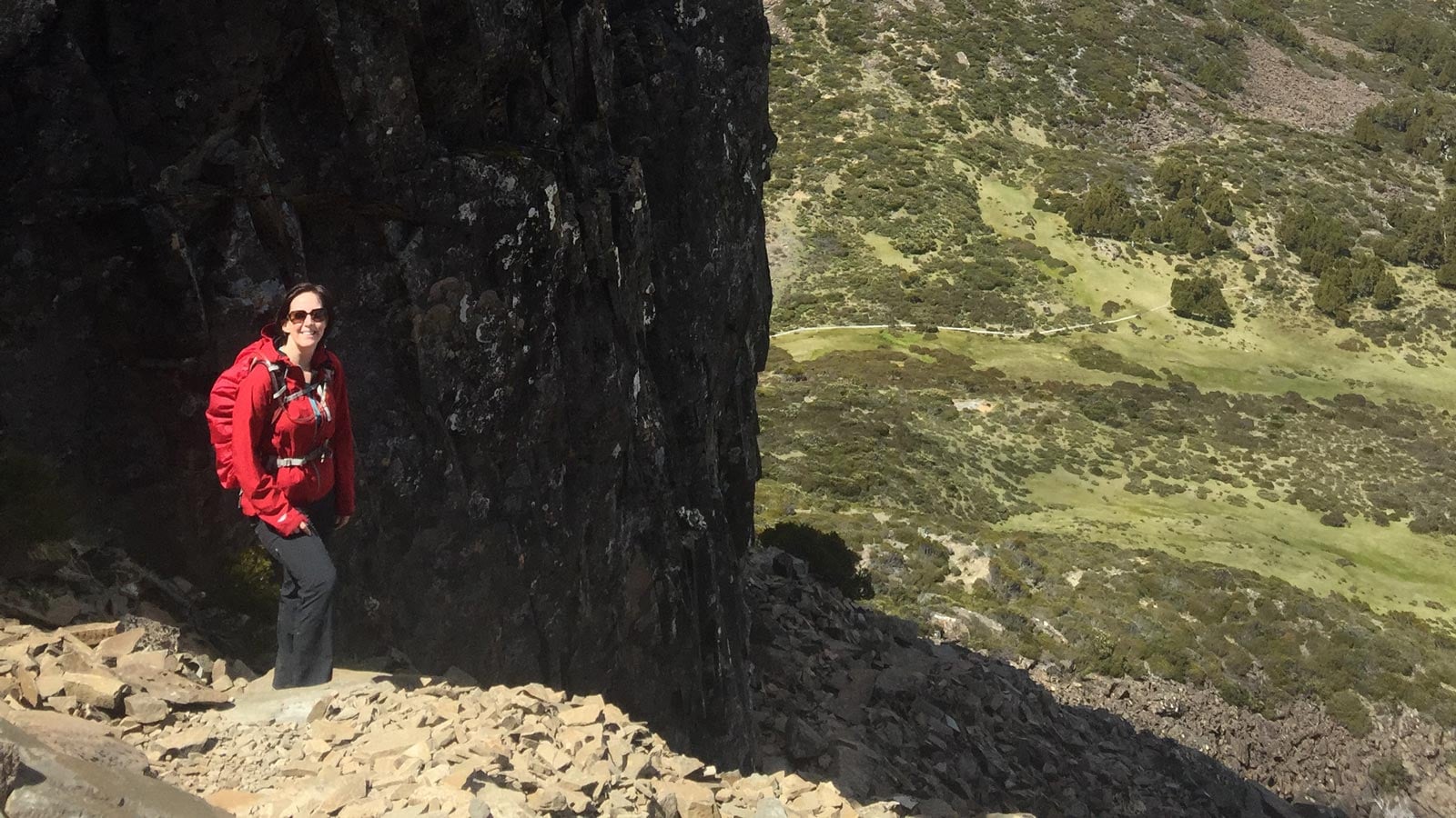 Hiker traversing a steep scree slope beneath a rocky cliff in alpine terrain