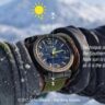 Close up of a wristwatch used for sun navigation in the southern hemisphere, with directional graphics overlaid against a blurred australian snow capped mountain background.