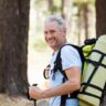 Hiker smiling at the camera while carrying a backpack with a rolled sleeping mat, trekking through an australian forest with another hiker in the background.