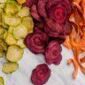 Assorted dehydrated vegetables including beetroot, zucchini, carrot and capsicum slices arranged on a white surface.