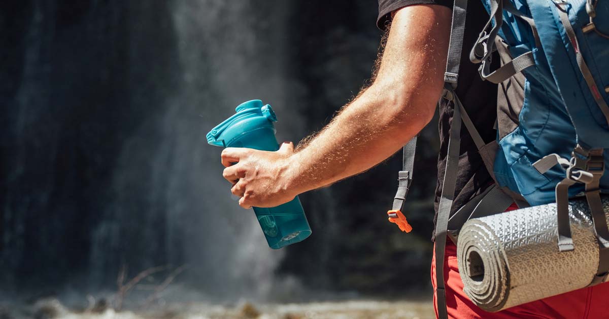 Hiker holding a water bottle while walking with a backpack outdoors