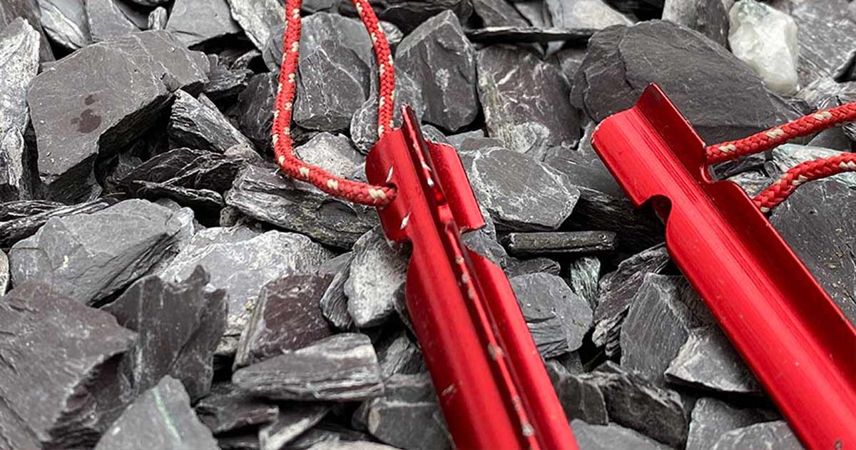 Red aluminium y-pegs with guy lines anchored in rocky ground, showing their three-sided profile and holding power.