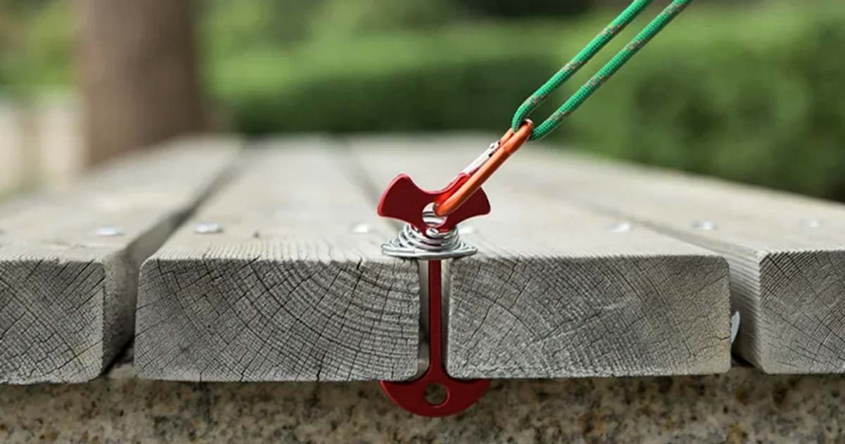 Fishbone platform tent anchor secured between wooden boards, with a guy line attached on a raised camping platform.