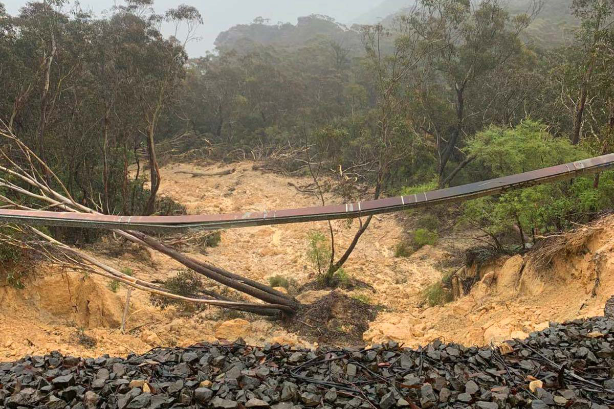 A landslide in an australian wilderness area, with debris and trees swept down a slope after heavy rain, obstructing the trail.