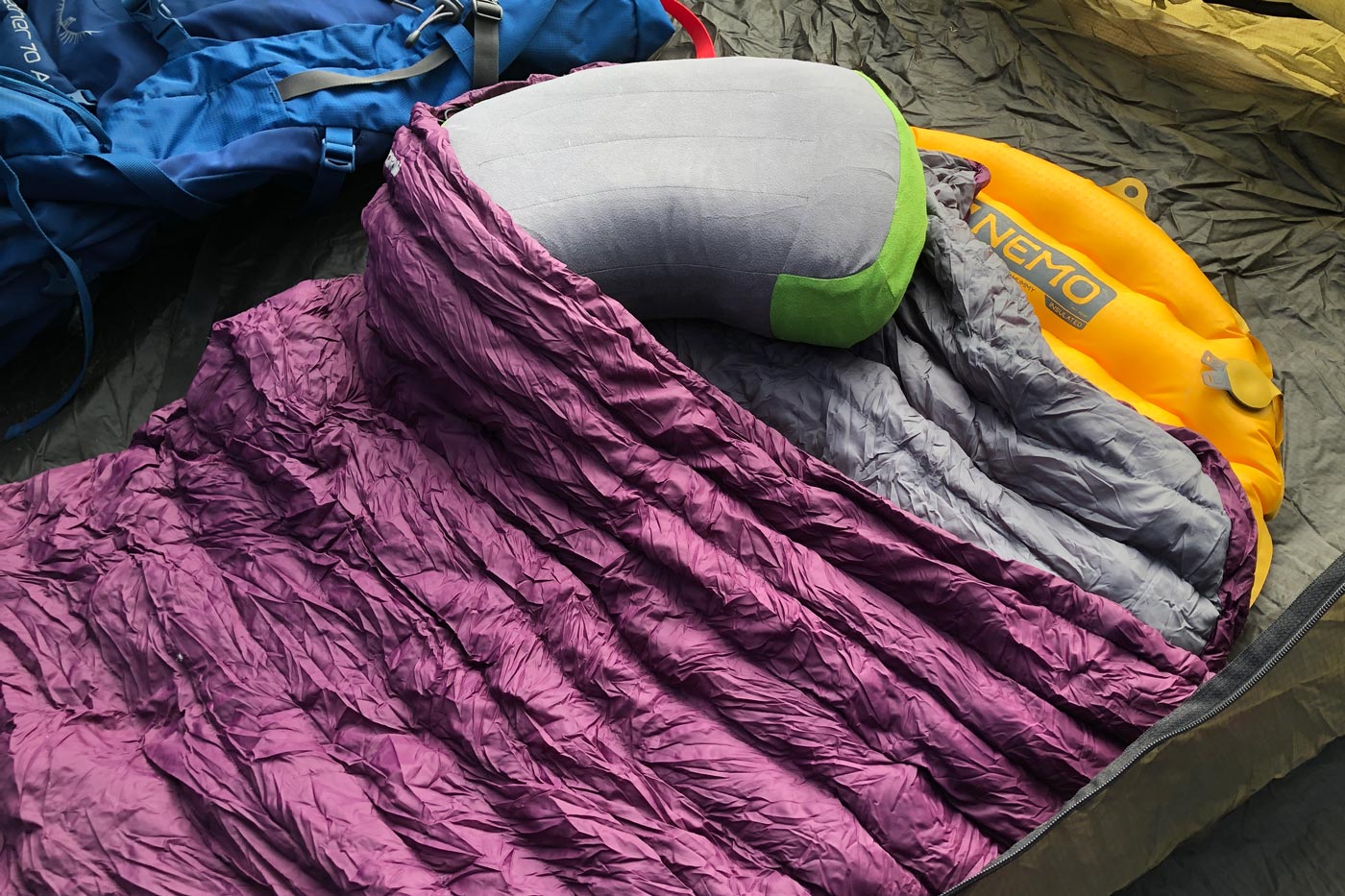 A sleeping bag with a purple outer layer, paired with a sleeping pad and pillow, showing the setup inside a tent.