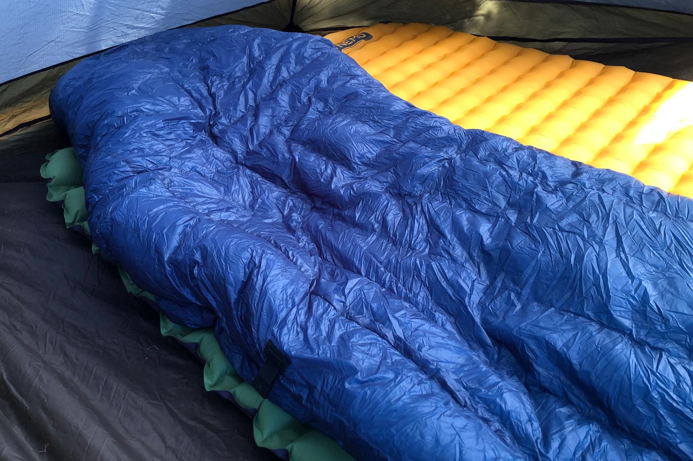 A blue quilt laid out on a sleeping pad inside a tent, showing the quilt’s design and insulation.