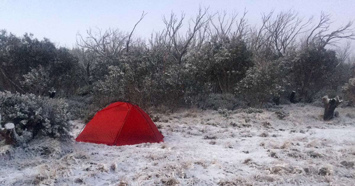 Red tent pitched in snowy alpine conditions during a multi-day hike