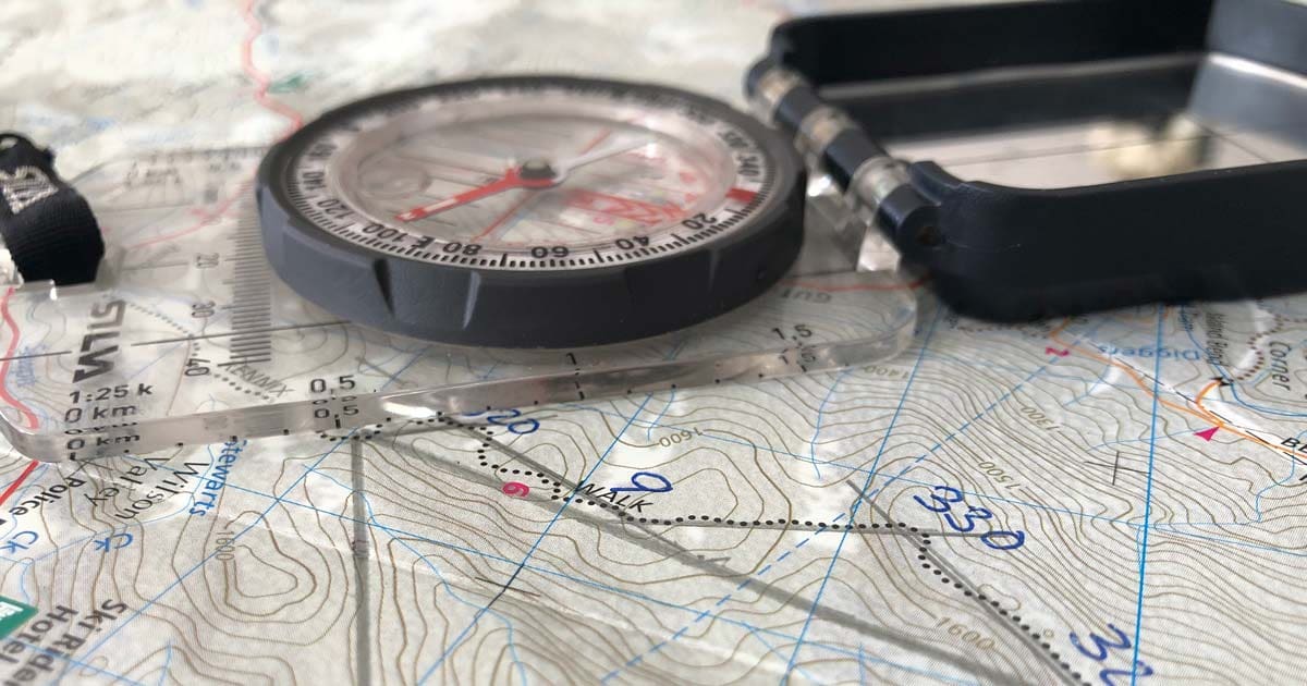 Hiker navigating with map and compass on a topographic map during a multi-day hike