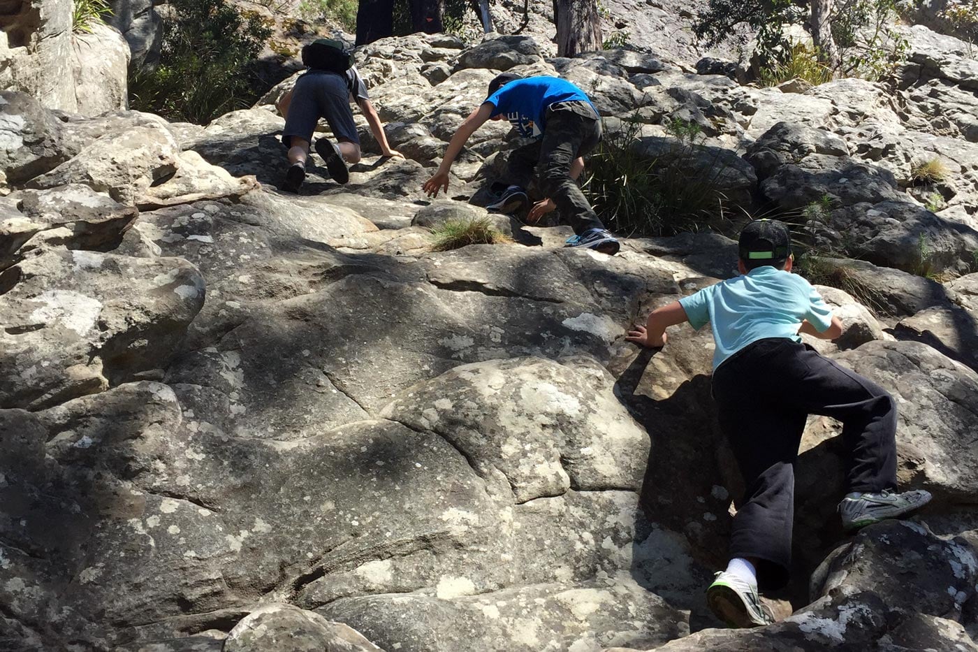 Footwear for rock scrambling Hikers scrambling up steep rock slabs using hands and feet, highlighting agility and freedom of movement typical of low-cut hiking shoes.
