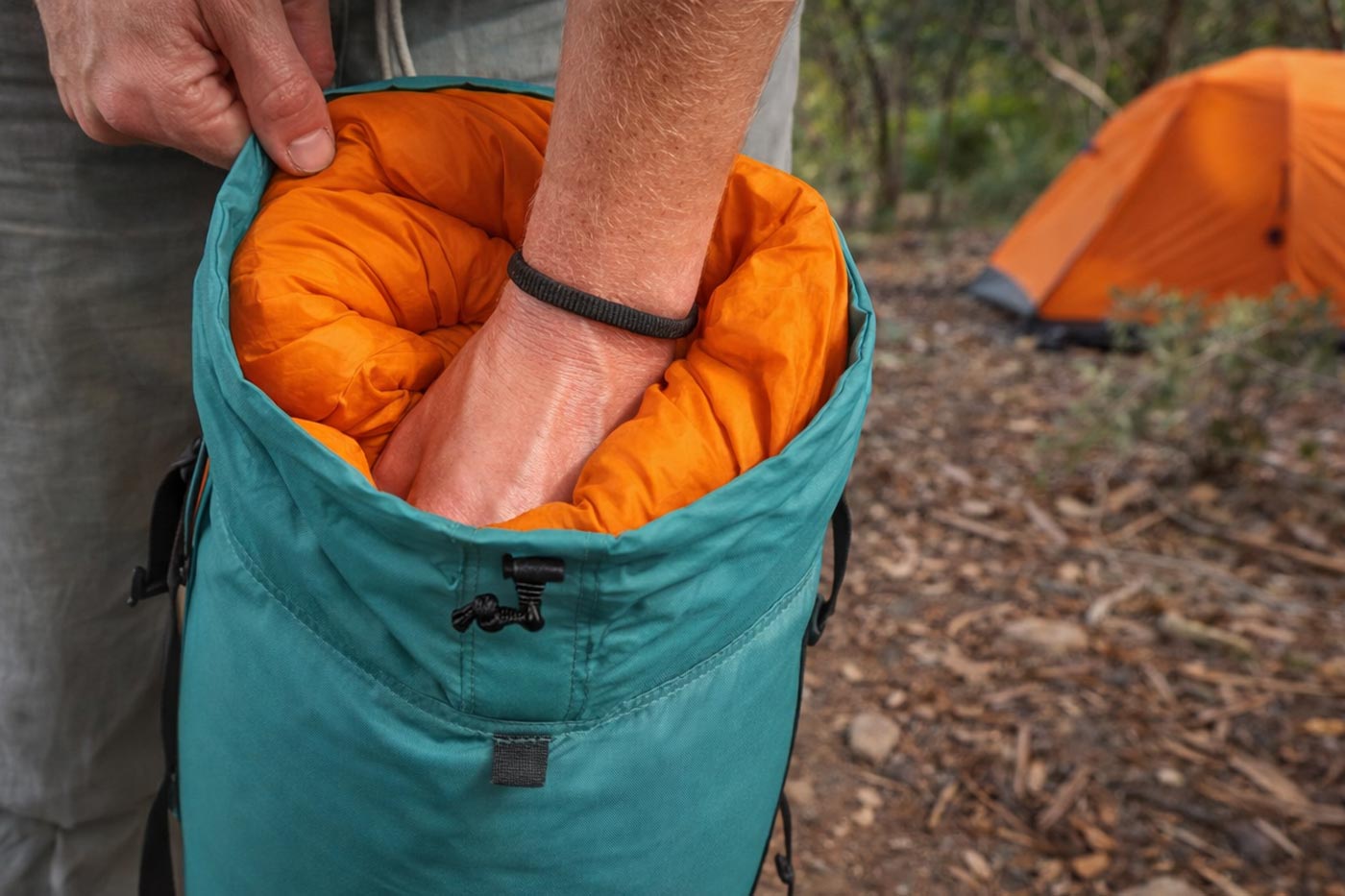 Stuffing a sleeping bag into a storage sack, ensuring compactness for easy packing for a hike.