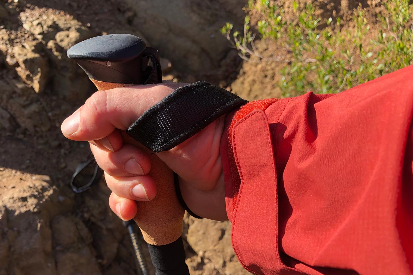 Hand holding a hiking pole with a cork grip and wrist strap, showing natural texture and grip comfort during use