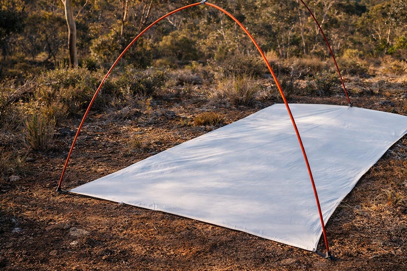 A tent footprint laid out on the ground with tent poles positioned above it before pitching.
