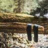 Hiking boots and black socks drying on a moss-covered fallen log over a forest stream, illustrating gear care and maintenance in the outdoors.