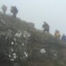 Hikers navigating rocky ridge in thick fog with limited visibility