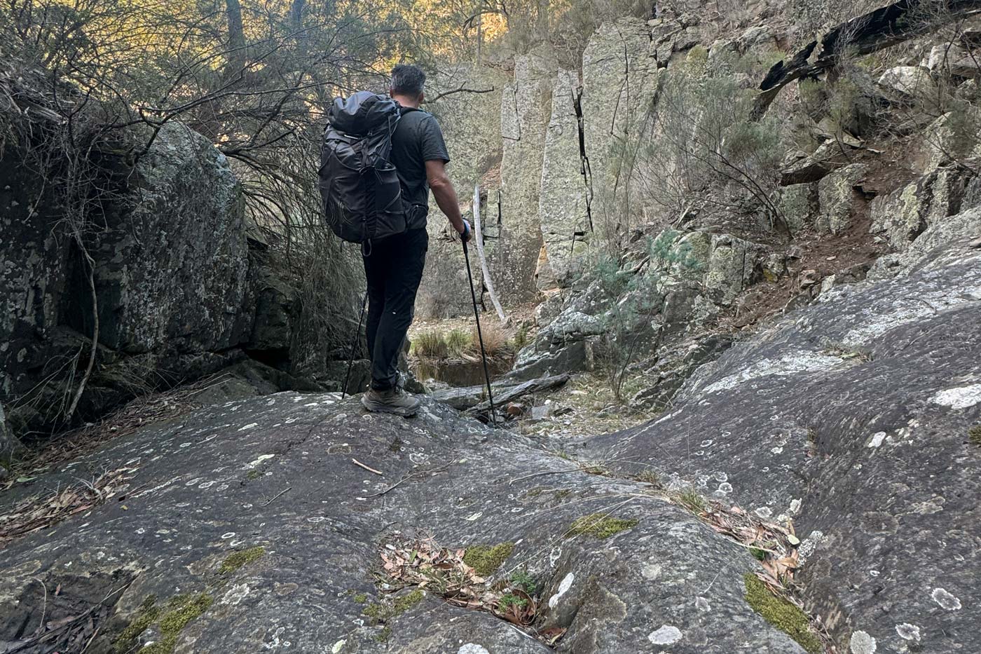 Hiker descending smooth rock slab with trekking poles wearing the north face offtrail hike lt mid gore-tex boots
