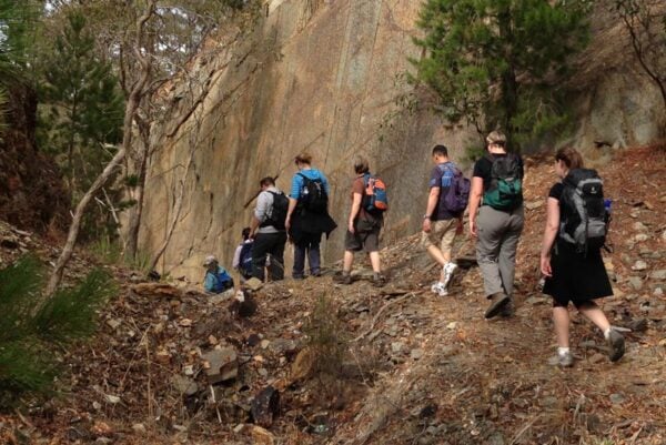 Group of hikers walking on a dry, exposed bush track in central victoria, highlighting heat, exertion, and increasing water demand during a midday hike