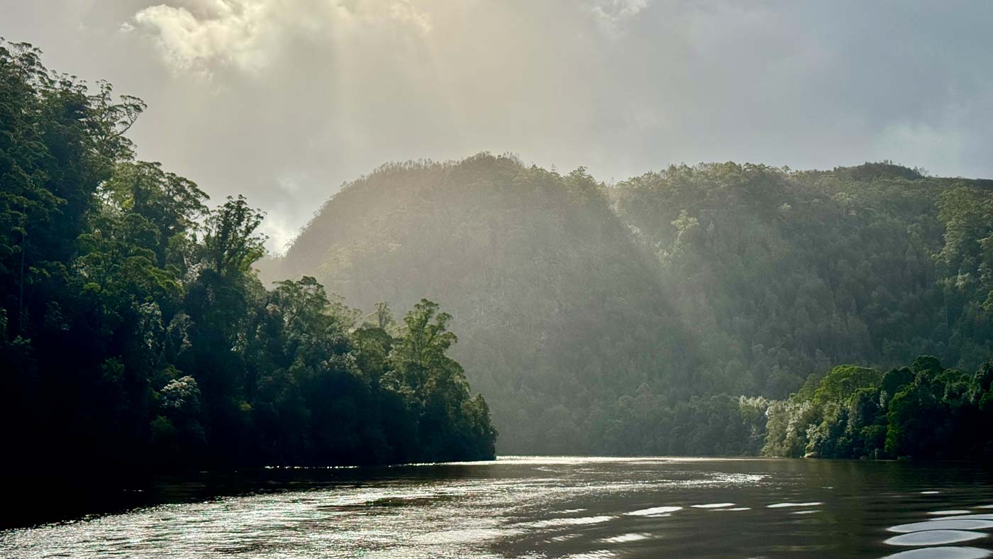Sunlight breaking through storm clouds over the forested banks of the pieman river near corinna in western tasmania.