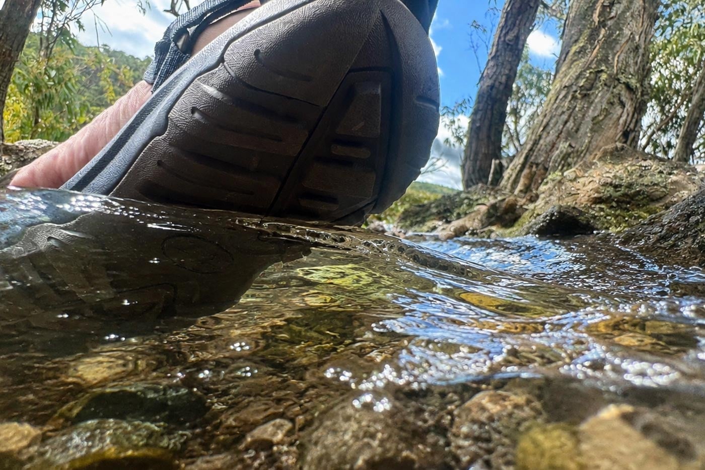 Low-angle shot of a zorali sandal partially submerged in a clear, flowing river, demonstrating its water-appropriate design.
