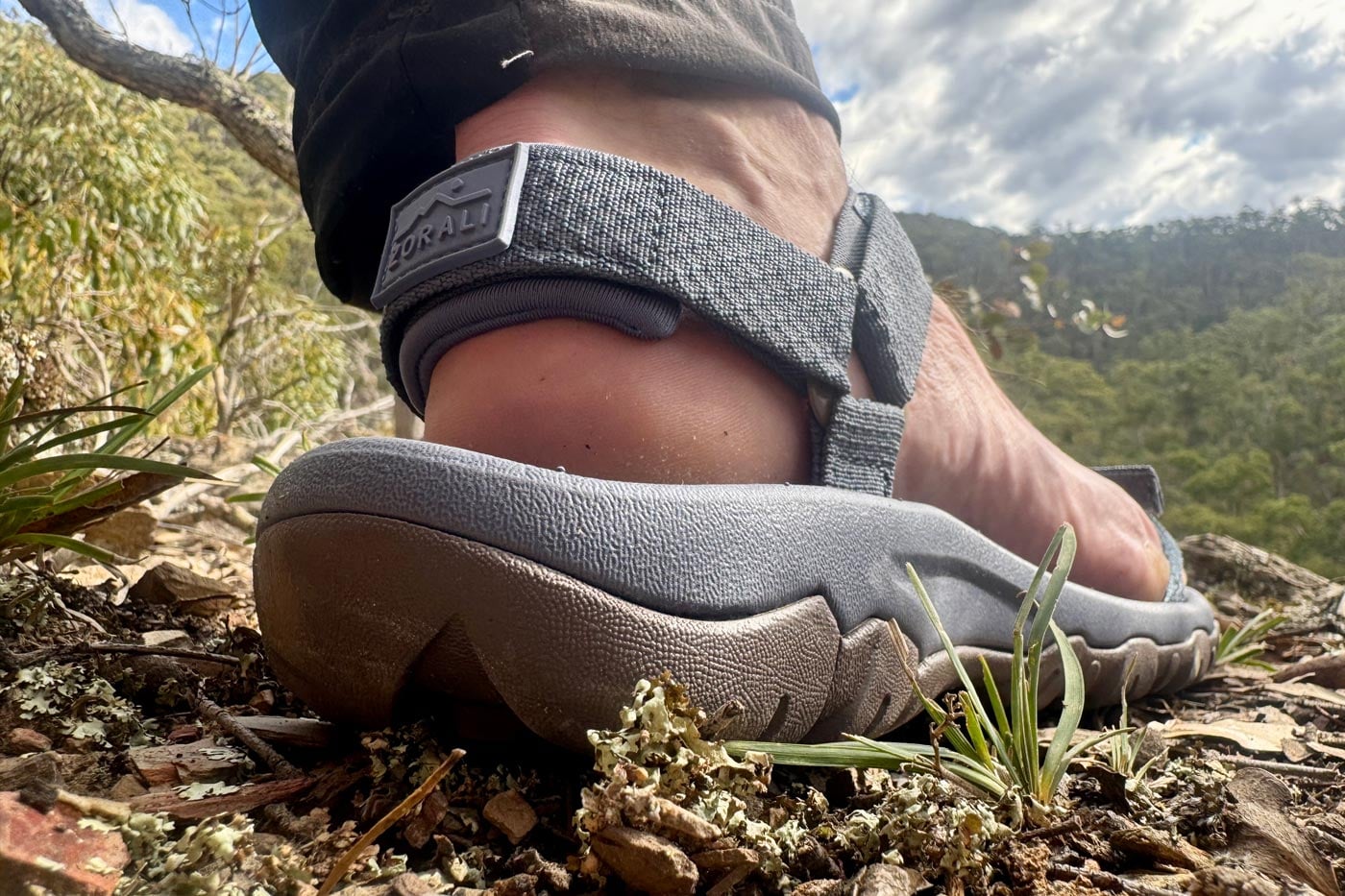 •close-up of a hiker's heel in a zorali sandal, highlighting the cushioned heel pad and the rubber zorali logo on the strap.
