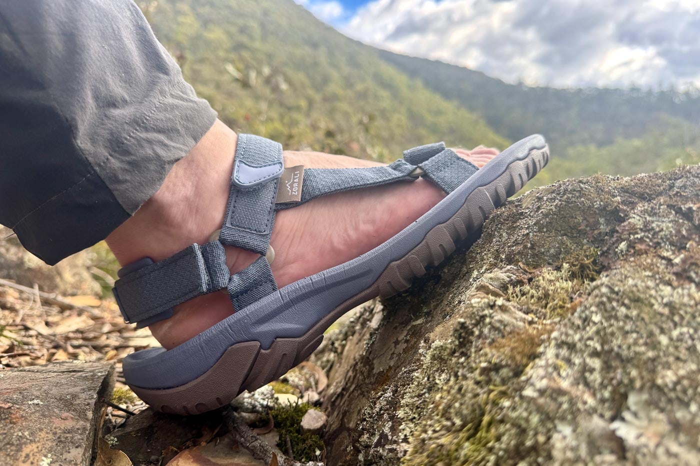 Side view of a zorali trailblazer sandal gripping a lichen-covered rock, showcasing the deep lug pattern of the tpr outsole.
