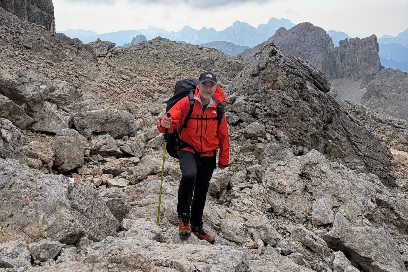 Hiker wearing a red waterproof jacket and carrying a backpack climbs across exposed rocky terrain in the italian dolomites.