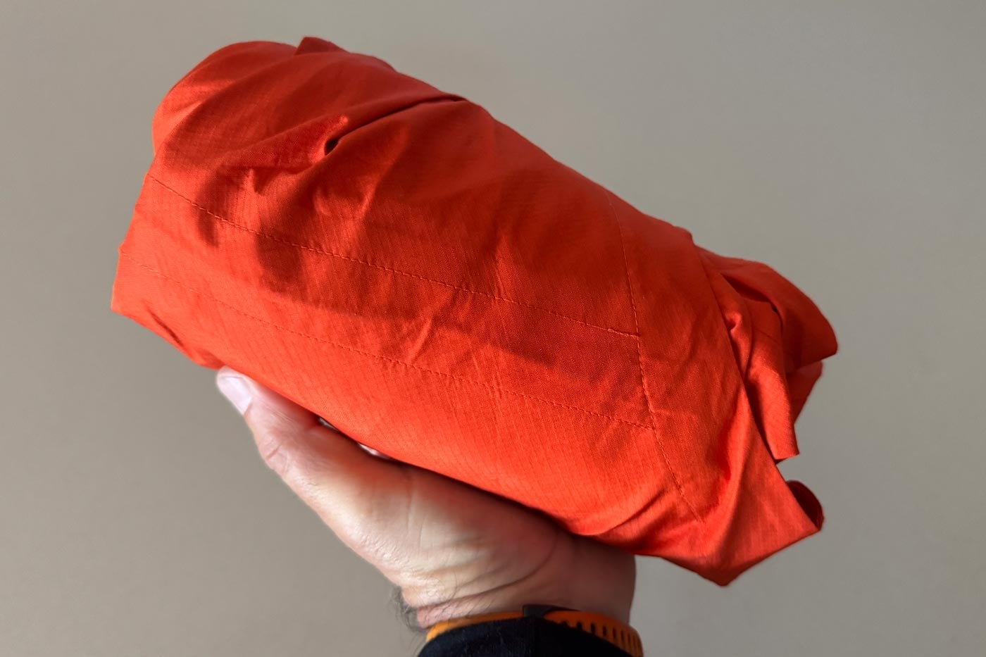 Compact red waterproof jacket folded and packed into its own pocket, showing the jacket’s packable design.
