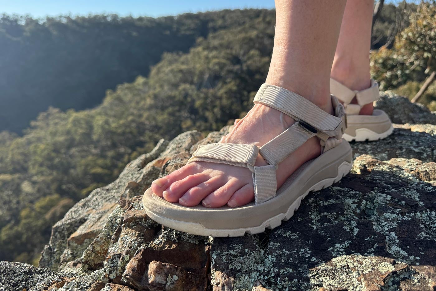 Teva Women's Hurricane XLT3 Sandal Review Hiker wearing beige strapped sandals with chunky soles, standing on a rocky cliff edge above bushland