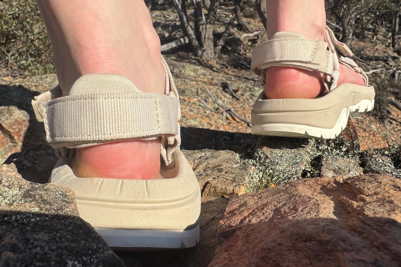 Teva Women's Hurricane XLT3 Sandal Review Close-up of feet wearing beige strapped hiking sandals with thick treaded soles, stepping on rocks in bushland