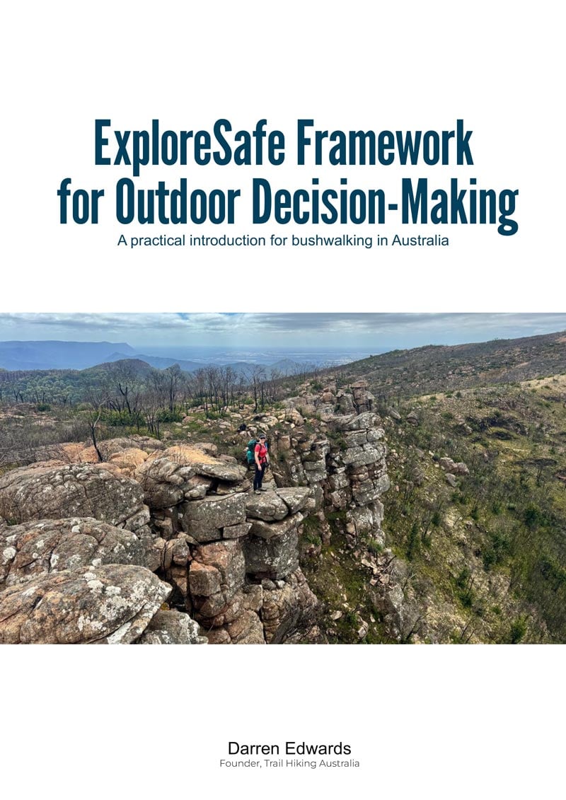 Hike Planning Checklist - Trail Hiking Australia A bushwalker with a red backpack stands atop rocky outcrops overlooking a forested valley and distant mountains under a partly cloudy sky