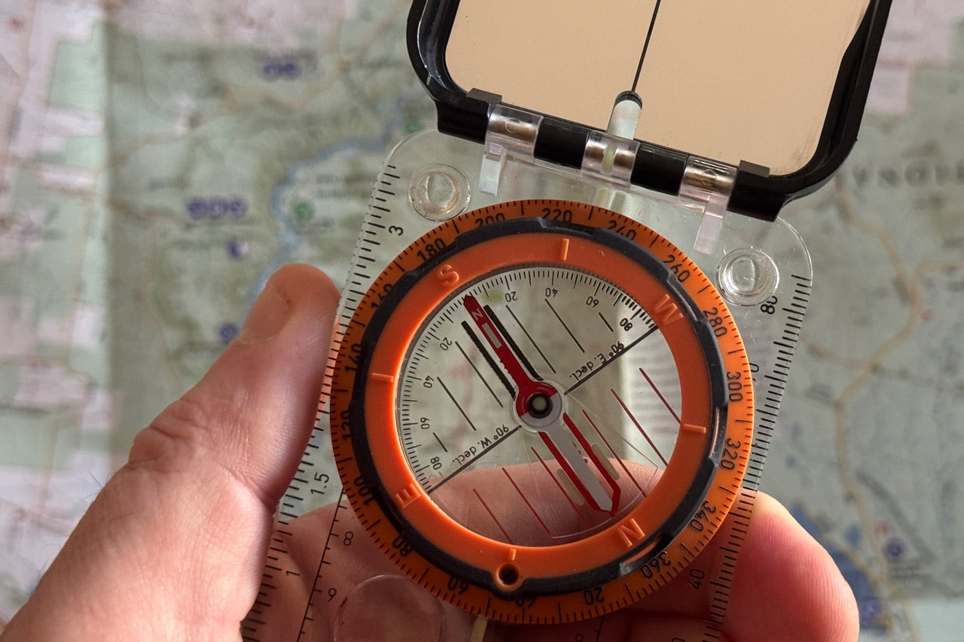 Understanding the Parts of a Hiking Compass Baseplate compass with mirror sighting lid held over a topographic map for navigation
